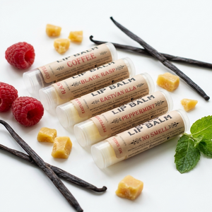 Five lip balm tubes with different scents on a white background with vanilla beans and raspberries.
